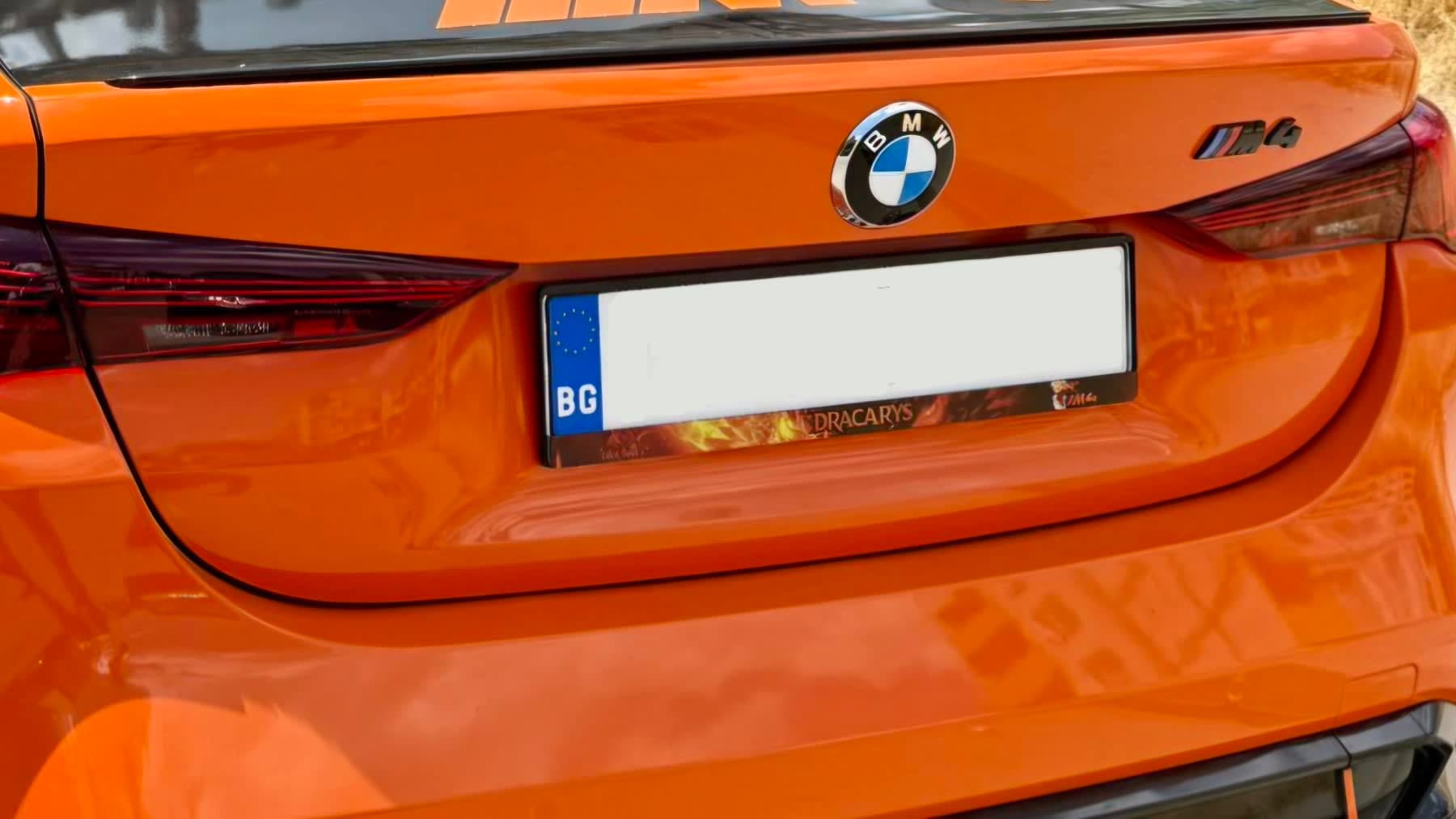 personalisierter DRACARYS Kennzeichenrahmen an einem orangefarbenen BMW M4 — Kennzeichenrahmen für BMW