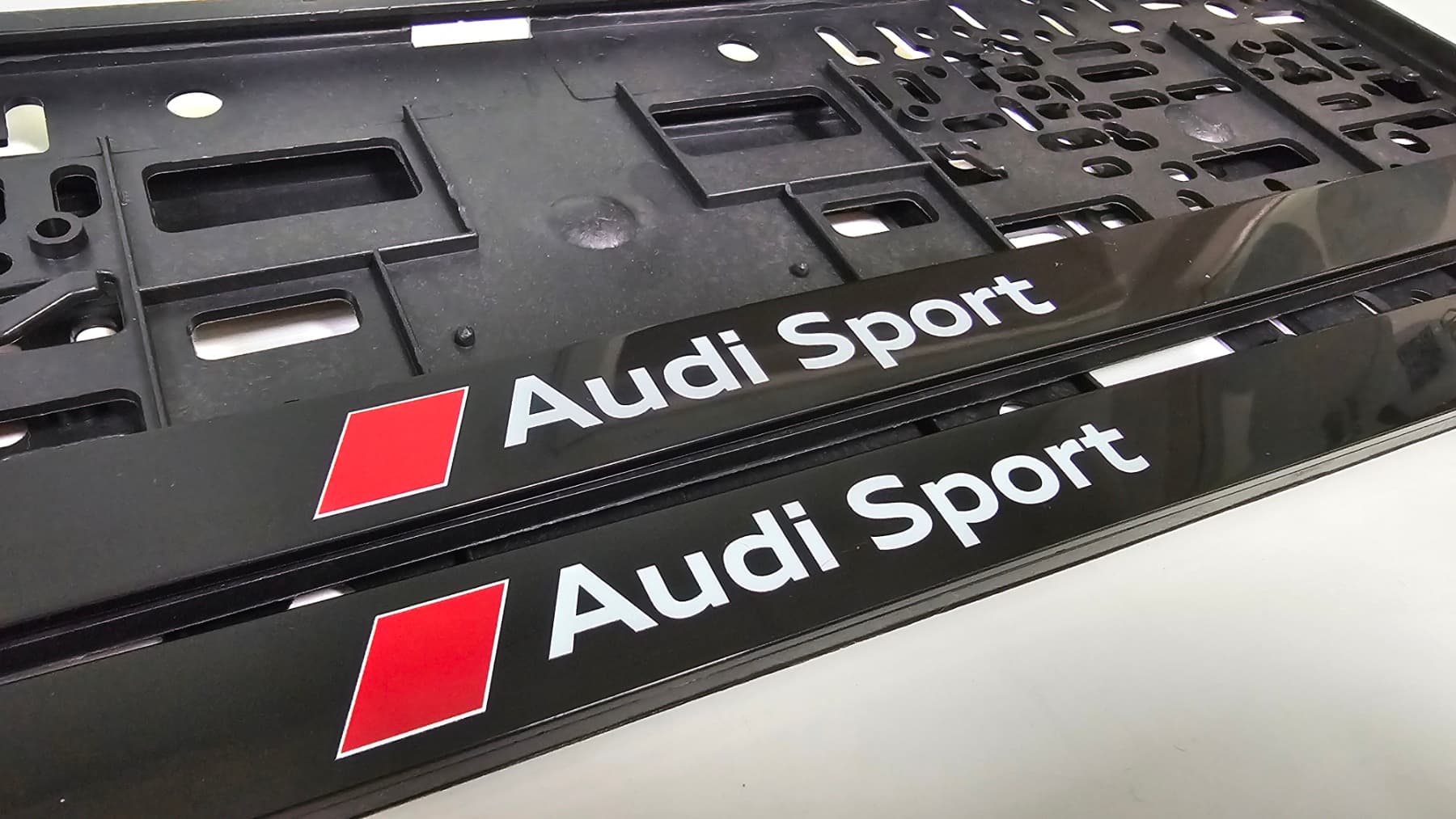 Audi license plate frame with white lettering and red rhombus — UV printing on black background